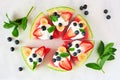 Healthy watermelon pizza with blueberries, strawberries, bananas and yogurt, above view over marble