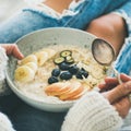 Woman in jeans and sweater eating oatmeal porriage, square crop Royalty Free Stock Photo