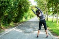 Healthy woman warming up before jogging run and relax stretching her arms and looking away in the road outdoor. Royalty Free Stock Photo