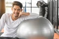 Healthy workout. Young cheerful man sitting on the yoga mat and exercising with ball in the gym Royalty Free Stock Photo