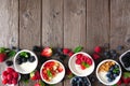 Healthy yogurt bowls with assorted berries and granola, bottom border against a wood background with copy space