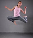 Healthy young muscular teenage girl skipping and dancing in studio. Child exercising with jumping on grey background.