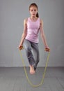 Healthy young muscular teenage girl skipping rope in studio. Child exercising with jumping on grey background.