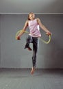 Healthy young muscular teenage girl skipping rope in studio. Child exercising with jumping on grey background.