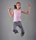 Healthy young muscular teenage girl skipping rope in studio. Child exercising with jumping high on grey background. Royalty Free Stock Photo