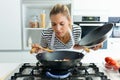 Healthy young woman cooking and smelling food in frying pan in the kitchen at home. Royalty Free Stock Photo