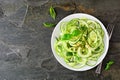 Healthy zucchini pasta topped with garlic and basil, top view on a dark slate background