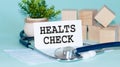 HEALTS CHECK - text on card on wooden table with stethoscope, medical mask and wooden blocks on background