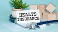 Healts insurance - text on card on wooden table with stethoscope, medical mask and wooden blocks on background