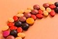 Heap of assorted brown, orange and red capsules on orange table.