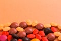 Heap of assorted brown, orange and red capsules on orange table.