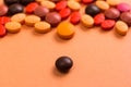 Heap of assorted brown, orange and red capsules on orange table.