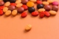 Heap of assorted brown, orange and red capsules on orange table.