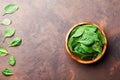 Heap of baby spinach leaves in wooden bowl on rustic stone table top view. Organic healthy food.