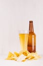 Heap beer junk snacks and golden lager beer in glass, brown bottle on soft white wooden background.