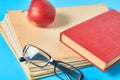 Heap of blank magazines, newspapers or some documents and modern glasses, red apple, book on blue desk Royalty Free Stock Photo