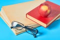 Heap of blank magazines, newspapers or some documents and modern glasses, red apple, book on blue desk Royalty Free Stock Photo