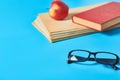 Heap of blank magazines, newspapers or some documents and modern glasses, red apple, book on blue desk