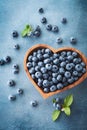 Heap of blueberry in heart shaped bowl on blue table top view. Organic superfood and healthy berry Royalty Free Stock Photo