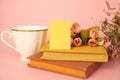 Heap of books, tea cup, flowers and blank paper card for message on pink background. Home leisure, resting at home concept.