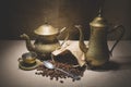 Heap of coffee beans in burlap sack with a vintage spoon and different vintage turkish coffeepots on canvas background