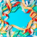 Heap of colorful measuring tapes in the form of frame on turquoise background. Top view of slim waist concept with copy space