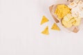 Heap different crispy golden snacks on craft paper, triangles nachos on soft white wood background, with copy space.