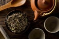 Heap of dried, raw white tea leaves in wooden bowl with teapot and cups on wooden table flat lay top view from above Royalty Free Stock Photo