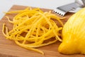 Heap of peeled lemon zest on wood chopping board next to half of peeled lemon and zester