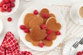 A heap of heart shaped pancakes on the white plate with raspberries on the white background