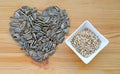 Heap of heart shaped raw sunflower seeds with a bowl of roasted seeds