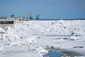 A heap of ice floes on the Amur River during the spring ice drift. Cranes of the river port and the buildings of the