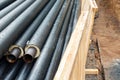 Heap of many new black insulated steel pipes at municipal construction site with wooden fencing around trench outdoors