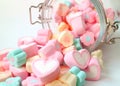 Heap of Pastel Color Heart Shaped and Flower Shaped Marshmallow Candies Scattered from a Glass Jar onto White Table Royalty Free Stock Photo
