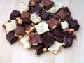 Heap of pieces of milk chocolate, white chocolate and dark chocolate with hazelnuts on a wooden background