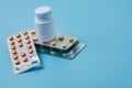 Heap of pills in blister packaging and plastic bottle lies on blue desk