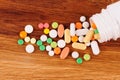 Heap of pills near the opened container on wooden desk