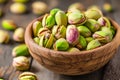 Heap of pistachios in wooden bowl on wooden background. Tasty pistachio nuts on kitchen table. Nutrition and diet concept