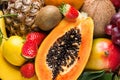 Heap of raw organic tropical and seasonal summer fruits berries halved papaya, coconut mango kiwi bananas pineapple strawberries