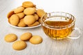 Heap of round biscuits in plate, transparent cup with tea, few cookies on wooden table Royalty Free Stock Photo