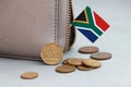 Heap of South African Rand coin money and mini South African flag stick on the leather wallet on grey background