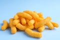 Heap of tasty cheesy corn puffs on light blue background, closeup view Royalty Free Stock Photo