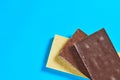 Heap of three various whole porous chocolate bars lies on blue table on kitchen. Space for text