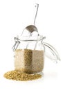 Heap of uncooked, raw freekeh or firik, roasted wheat grain, in glass storage jar with metal scoop over white Royalty Free Stock Photo