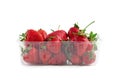 Heap of vivid saturated ripe red strawberries laying in big plastic transparent container and one big berry laying near