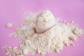 Heap of whey protein powder with plastic spoon on pink background