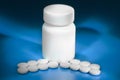 Heap of white pills and a white pill bottle on blue background Royalty Free Stock Photo