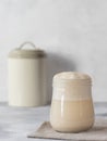 Heaping jar of sourdough starter yeast, a container with flour in the background. Royalty Free Stock Photo