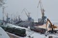 Heaps of coal in the port. Cranes unload train freight cars coal loading. Blue and yellow port reloading cranes Royalty Free Stock Photo