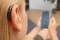 Hearing impaired woman working with smartphone. Close up of blonde woman wearing hearing aid on ear and pressing button while